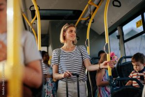 Group of people commuting by bus. The focus is on the young woman with suitcase holding the railing.